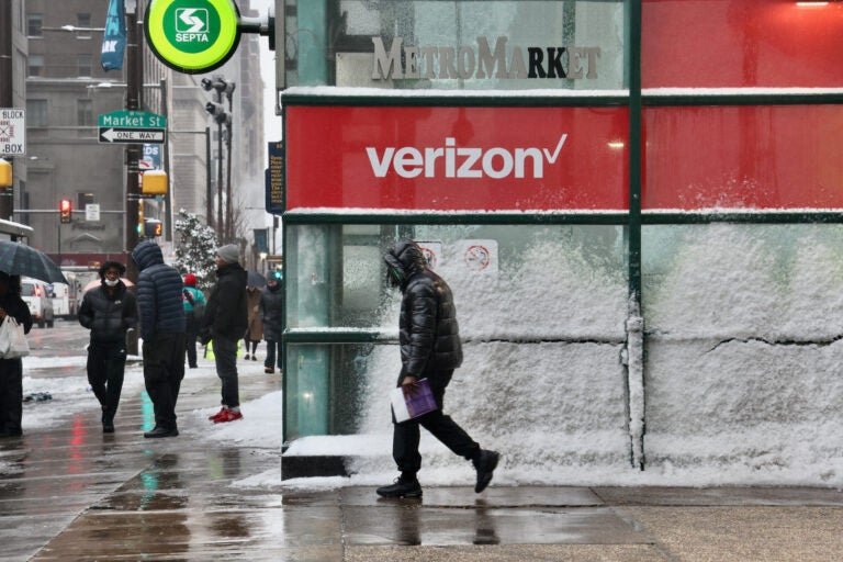 A pedestrian passes by a Verizon store with windows coated in frost and snow.