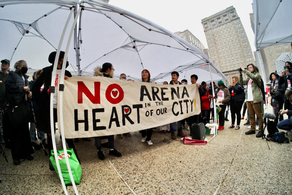 People hold up a sign that reads "No arena in the heart of our city"