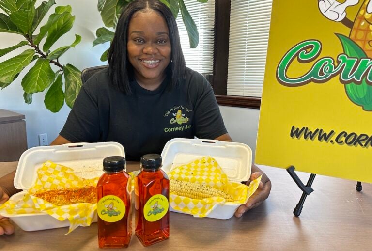 Nija Wiggins poses, smiling, with some of her corn on the cob specialties in front of her.