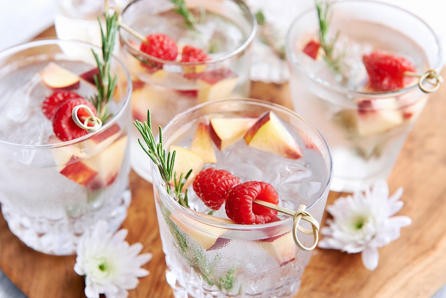 Fruity refreshing mocktails being served on a wooden tray decorated with flowers, raspberries, sliced apples and garnish.