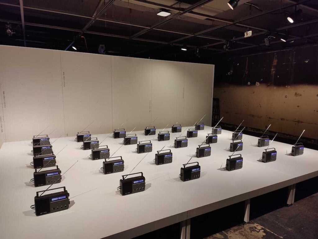 An art installation featuring rows of radios playing the U.S. national anthem in different languages.