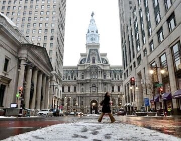 A person crossing the street in front of Philadelphia City Hall with snow on the ground.