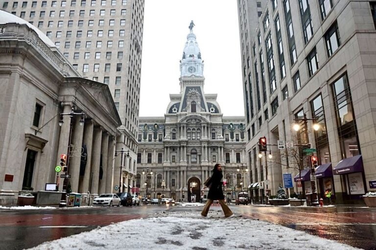 A person crossing the street in front of Philadelphia City Hall with snow on the ground.