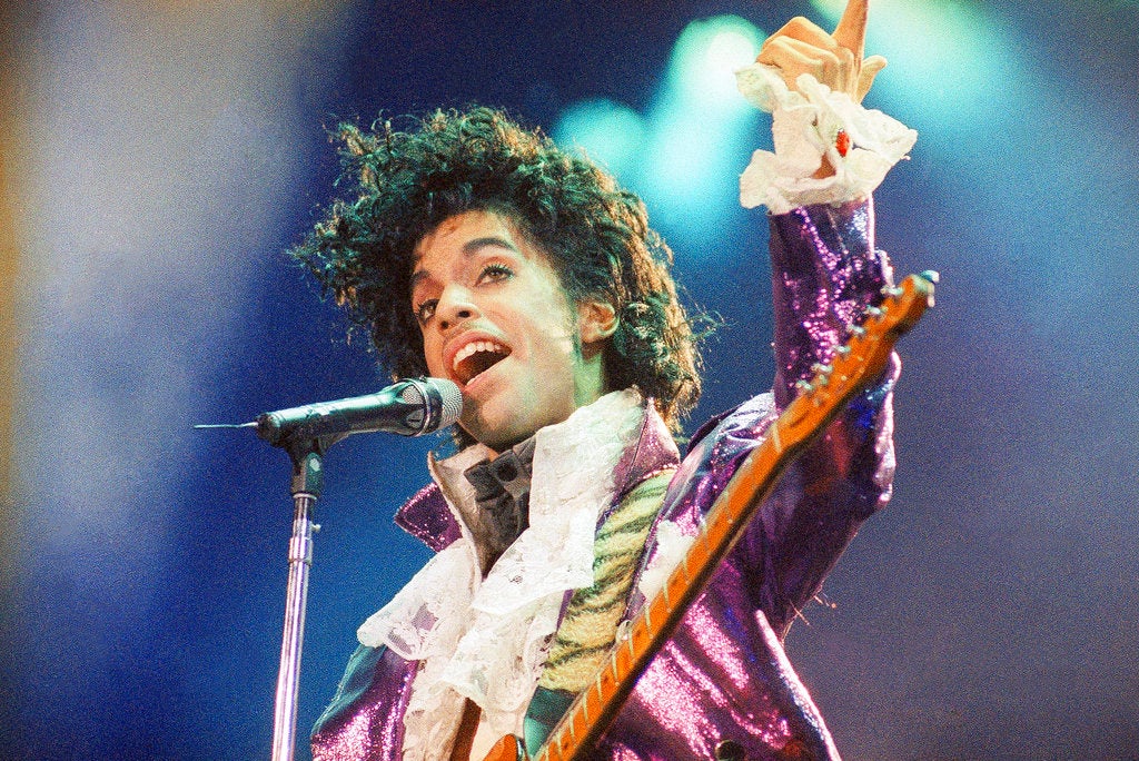 Prince sings into a microphone while performing