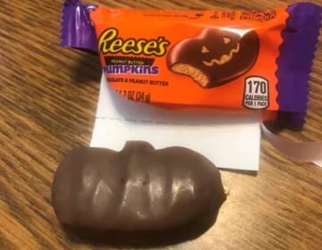 A Reese's Peanut Butter Pumpkin with no carved-out face next to the open wrapper with a jack-o'-lantern design.