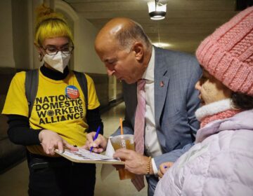 Councilmember Mark Squilla signs a pledge to support workers as members of the Domestic Workers Alliance look on.