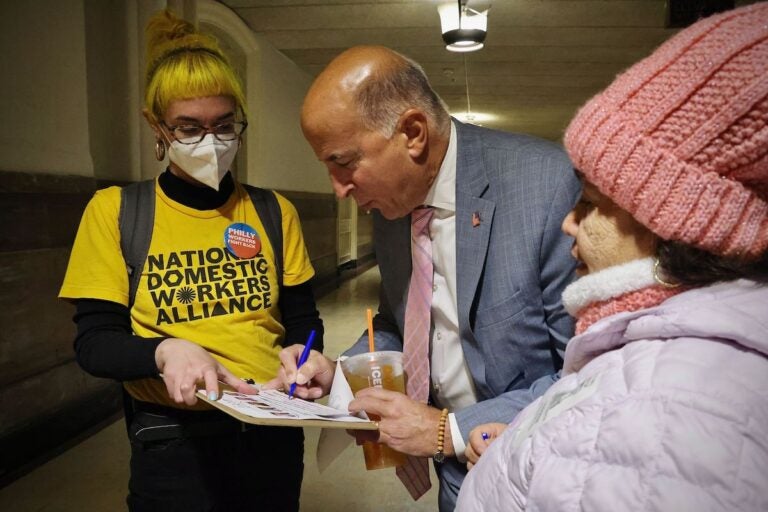 Councilmember Mark Squilla signs a pledge to support workers as members of the Domestic Workers Alliance look on.