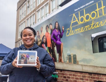 Ebonie Thorpe, a 6th grade teacher at the James R. Ludlow School in Philadelphia, holds up a lunchbox in front of an advertisement for Abbott Elementary