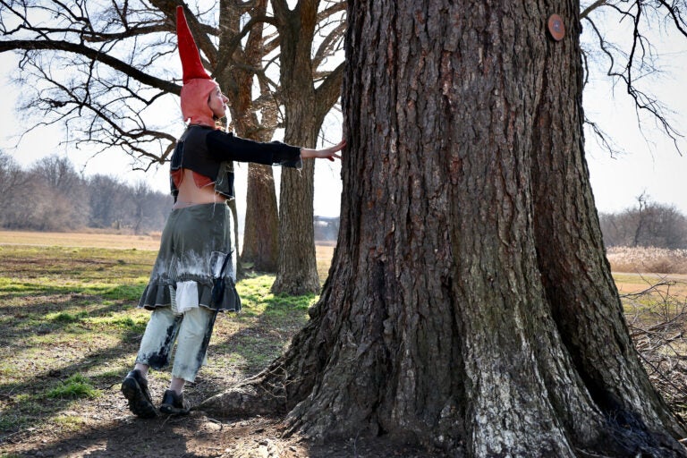 Alex Tatarsky, in gnome attire, stands next to a tree