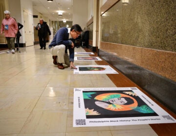 Tu Huynh, program manager for the Philadelphia Office of Arts, Culture, and the Creative Economy, kneels beside a portrait of Philadelphia artist and educator Moe Brooker