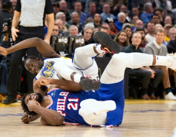 Golden State Warriors forward Draymond Green (23) falls over Philadelphia 76ers center Joel Embiid (21) on an offensive foul by Embiid during the first half of an NBA basketball game, Tuesday, Jan. 30, 2024, in San Francisco.