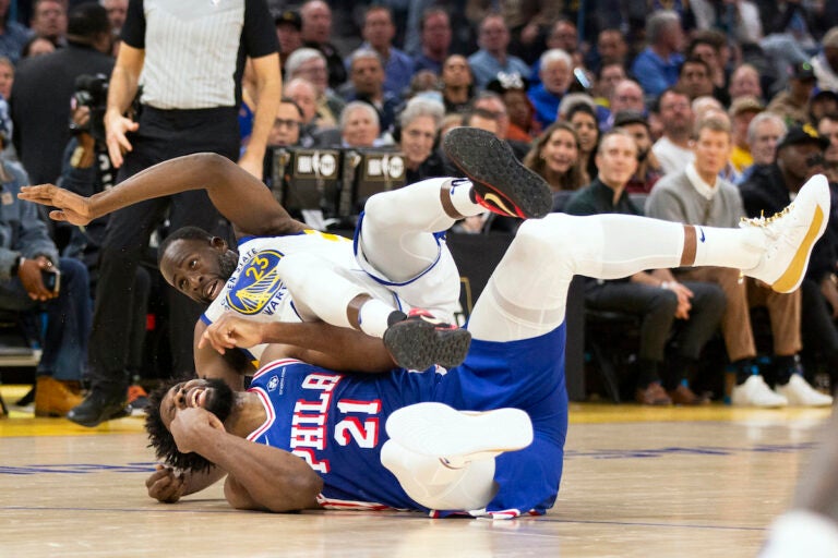 Golden State Warriors forward Draymond Green (23) falls over Philadelphia 76ers center Joel Embiid (21) on an offensive foul by Embiid during the first half of an NBA basketball game, Tuesday, Jan. 30, 2024, in San Francisco.