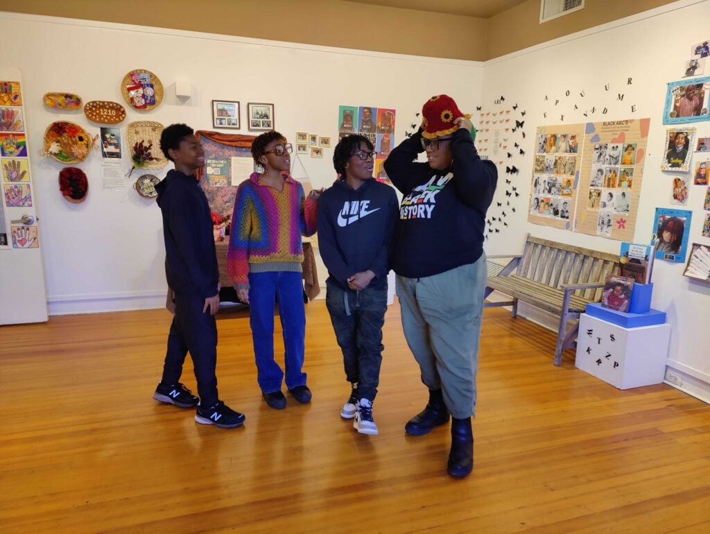 Sabraiya Shipley pulls on a hat crocheted for her by Ana Gadson, one of her collaborating students, joined by Jaheim Faison, Gadson, and Mukhlis Jabbaar.