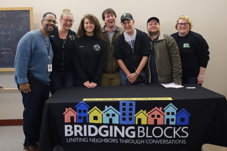 Team members pose for a photo behind a table with a sign reading Bridging Blocks