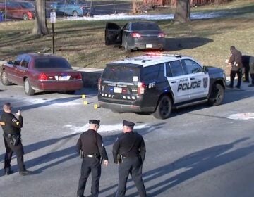 Officers stand around a police car at the scene of a shooting.