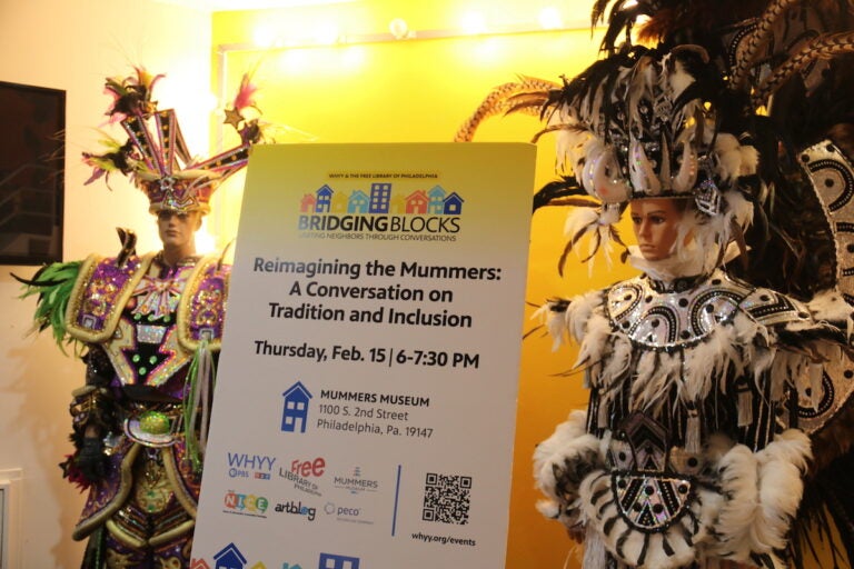 A sign advertises the Bridging Blocks discussion at the Mummers Museum with two mannequins dressed in Mummers outfits on either side