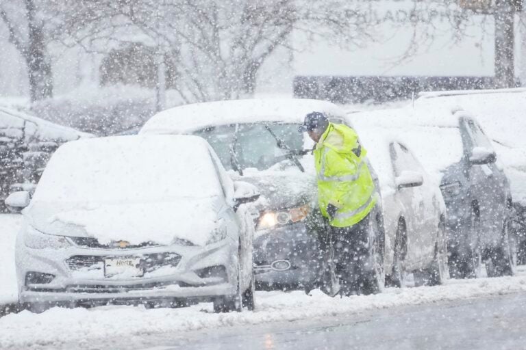 A person cleans off a car during a winter snow storm in Philadelphia, Tuesday, Feb. 13, 2024.
