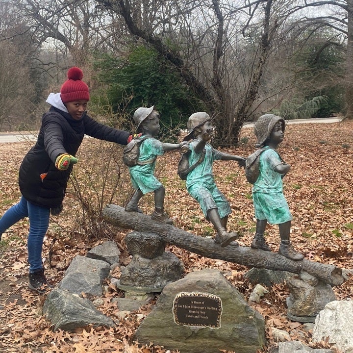 A person poses for a photo with a statue of three children walking on a log