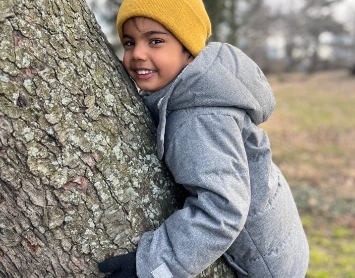 A child poses for a photo while hugging a tree.