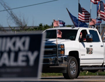 A sign reads Nikki Haley. In the background is a truck with the U.S. flag and flags supporting Trump