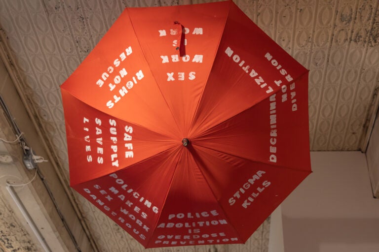 An umbrella with text on it hangs from a ceiling in an art installation.