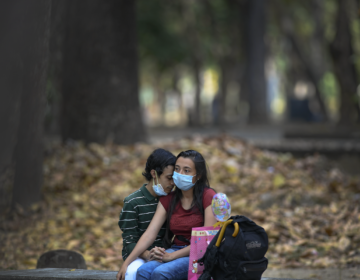 A couple wearing masks curb the spread of the new coronavirus sit together at a public park in on Sunday, Feb. 14, 2021. (AP Photo/Matias Delacroix)
