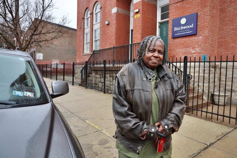 June Burris poses for a photo outside of a building with a sign that reads 