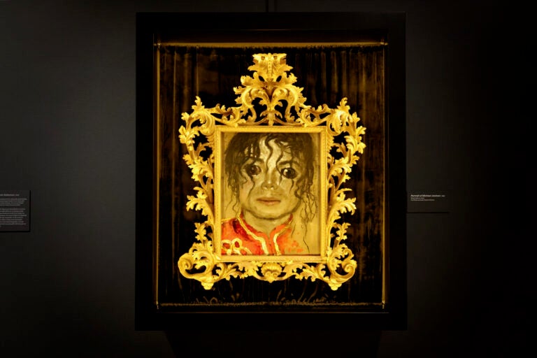 Jamie Wyeth's portrait of pop icon Michael Jackson floats in the darkness surrounding it's painted gold frame. (Emma Lee/WHYY)