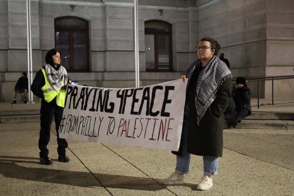 Volunteer safety marshals hold a sign expressing solidarity with the people of Gaza while watching over Muslim devotees in prayer outside City Hall.