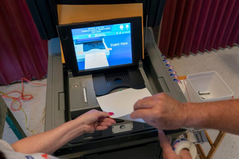 File photo: A polling judge (right) helps guide a voter's ballot into a voting machine during the Pennsylvania primary election, at Mont Alto United Methodist Church in Alto, Pa., on May 17, 2022.