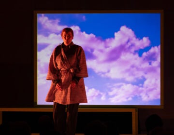A performer stands in front of a screen with clouds