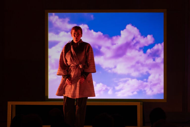 A performer stands in front of a screen with clouds