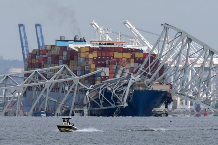 A boat moves past a container ship as it rests against wreckage of the Francis Scott Key Bridge on Tuesday, March 26, 2024, as seen from Pasadena, Md