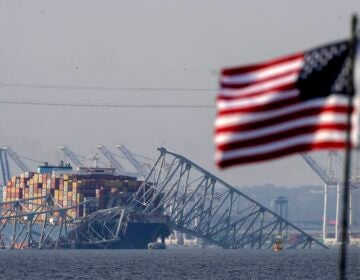 An American flag flies on a moored boat as the container ship Dali rests against wreckage of the Francis Scott Key Bridge, Tuesday, March 26, 2024, as seen from Pasadena, Md.