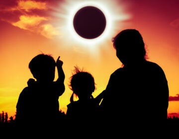 Silhouette back view of family sitting and relaxing together. Boy point to solar eclipse on gold sky background. Happy family spending time together. Outdoor.