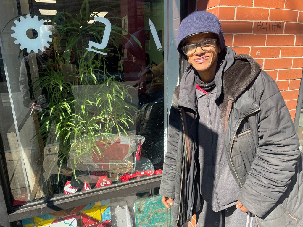 Althea Wilson posing for a photo with her painted rocks visible inside the window.