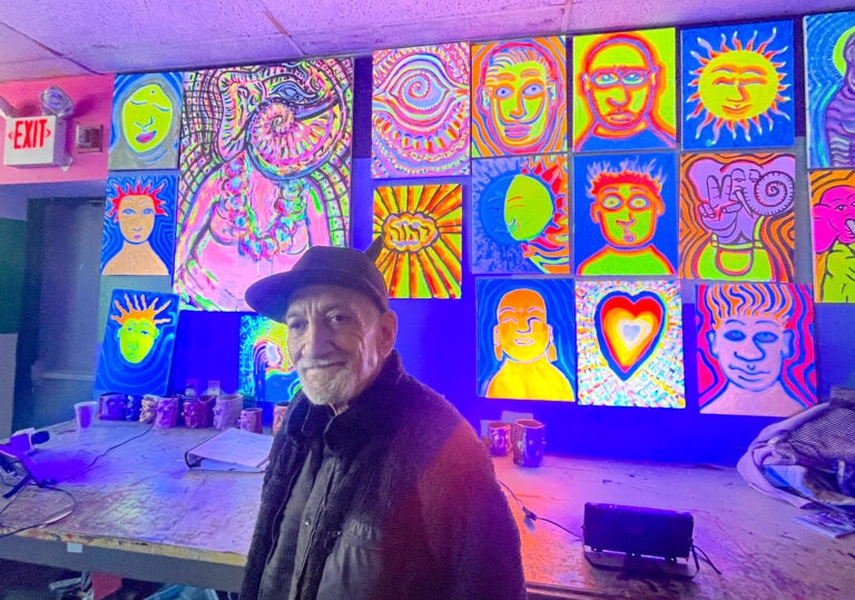 Ken Segal standing in front of a wall of brightly colored artworks
