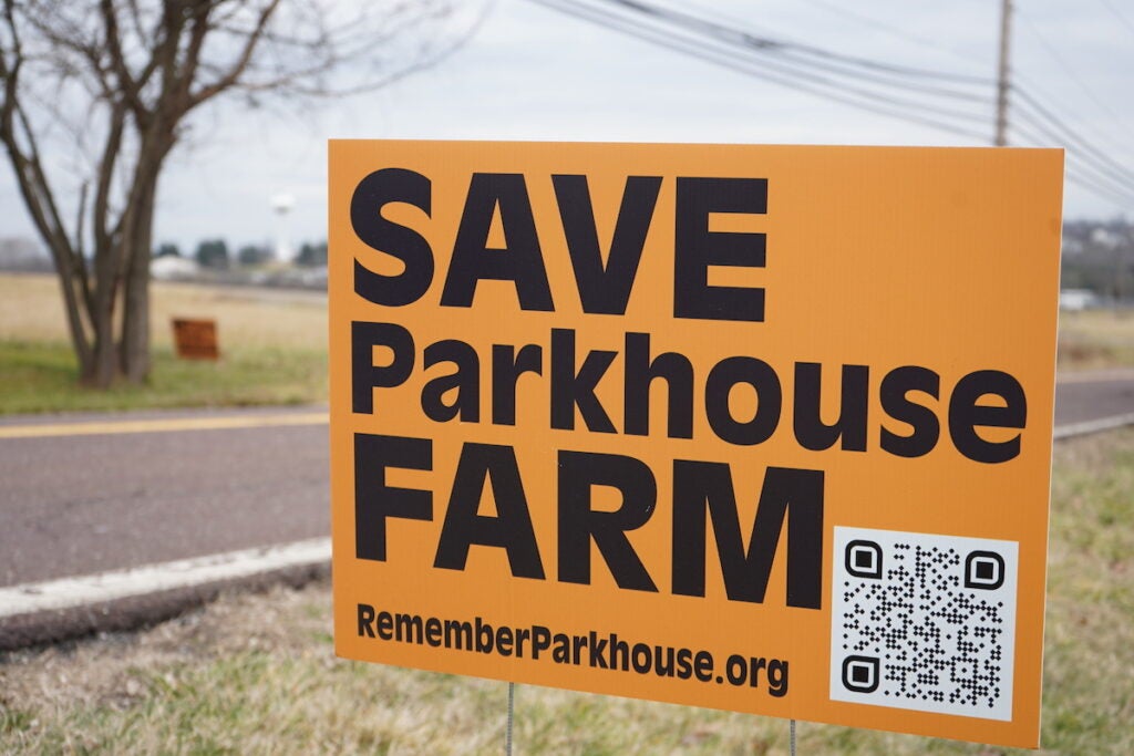 A sign on the side of the road reads "Save Parkhouse Farm" and has a QR code and a website printed below, reading "RememberParkhouse.org"