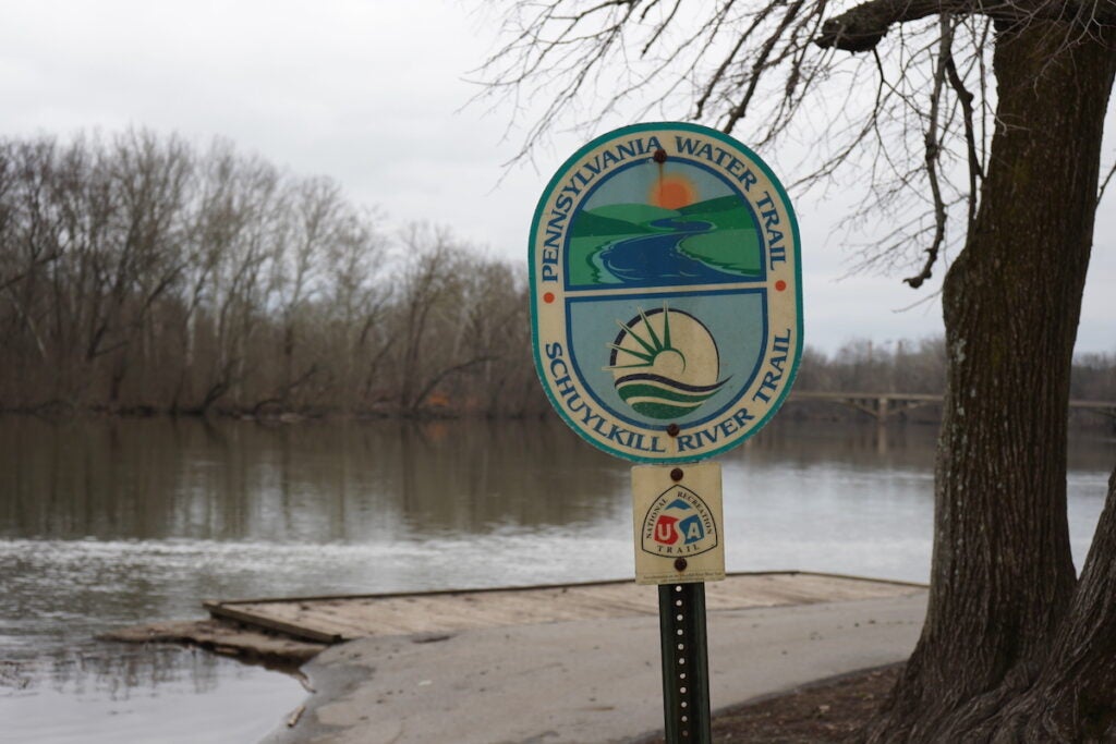 A sign in front of a body of water reads "Pennsylvania Water Trail Schuylkill River Trail"