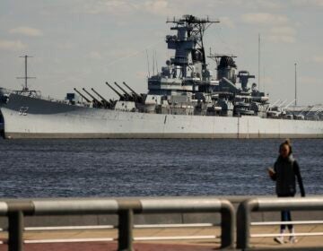 A person walks in Philadelphia across the Delaware River from the USS New Jersey in Camden, N.J., Tuesday, March 19, 2024.