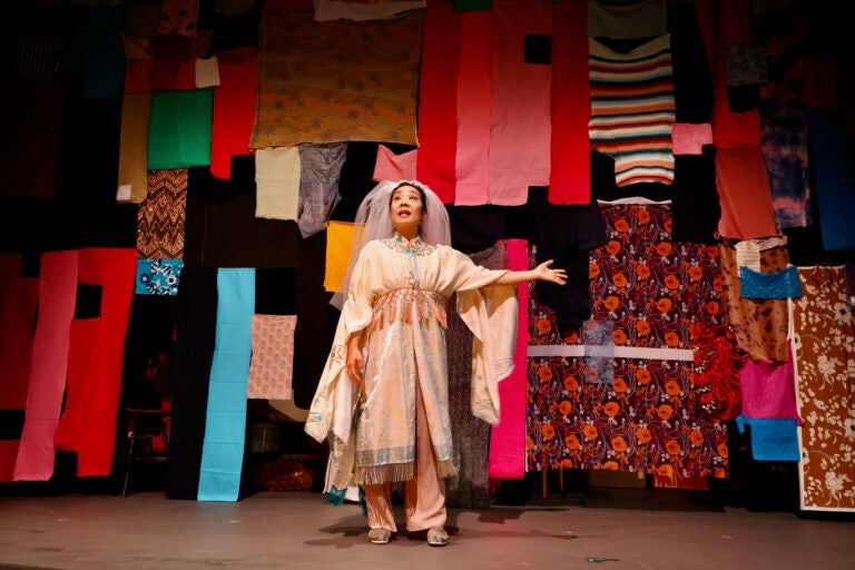 Bi Jean Ngo portrays Shen Te in ''The Good Person of Setzuan'' at Wilma Theater, performing in front of a curtain made of fabric scraps, hand-sewn by set designer Steven Dufala. (Emma Lee/WHYY)
