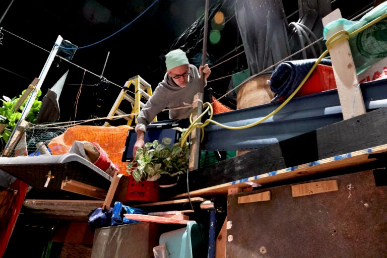 Set desinger Steven Dufala arranges objects in the shantytown set of ''The Good Person of Setzuan. Dufala built the set from recycled materials. (Emma Lee/WHYY)