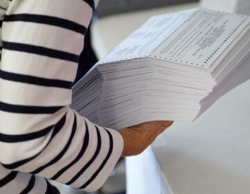 A woman is holding a stack of mail ballots