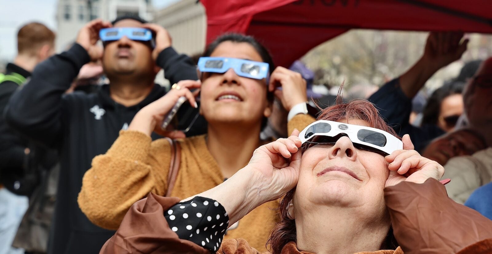 Three people are seen holding up eclipse glasses as the eclipse streaks across Philadelphia