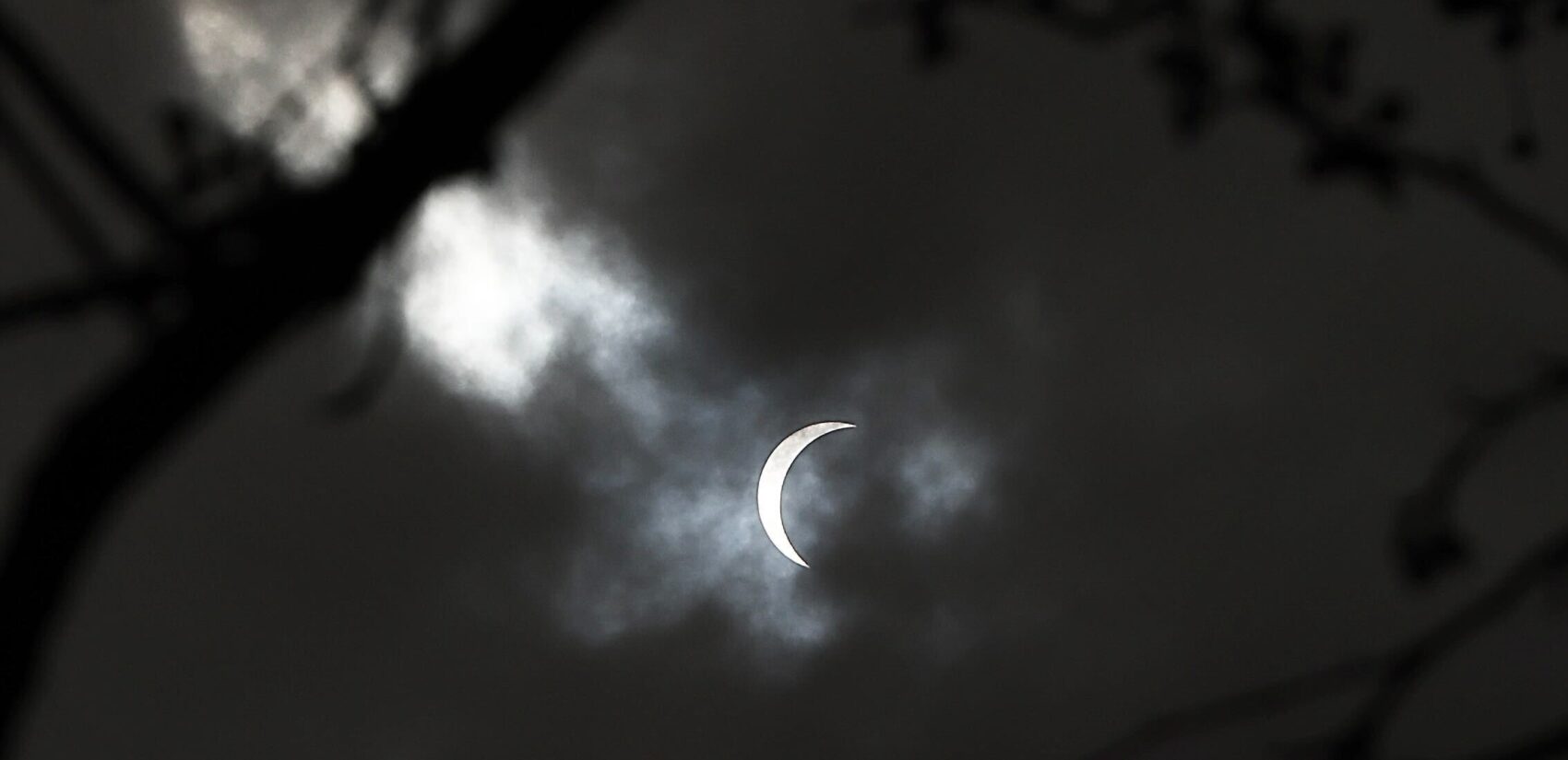 A sliver of sun is visible through a screen of clouds to viewers watching the solar eclipse outside the Franklin Institute in Center City Philadelphia.