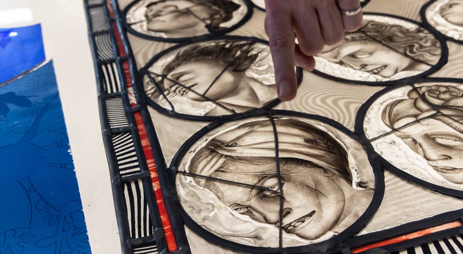 Judith Schaechter points to her work on her desk, showing faces