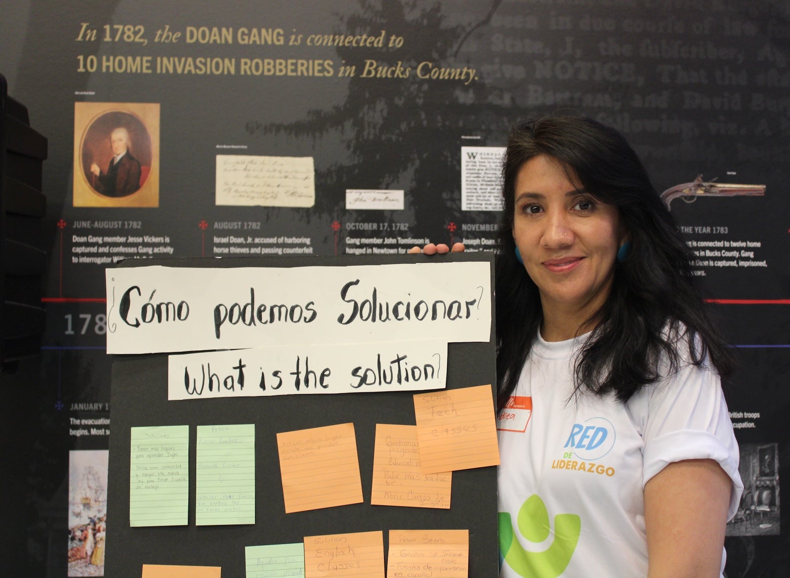 Andrea Lawton appears next to a poster that says, ''Como podemos solucionos, what is the solution''