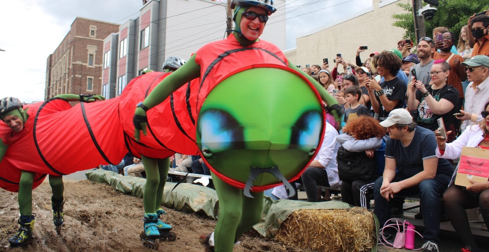 Kensington Derby participants dressed as a caterpillar on roller skates ride through the mud pit