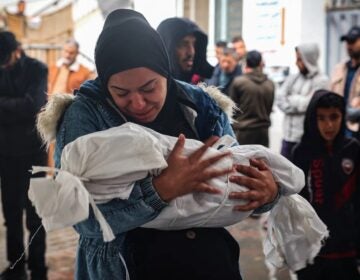 A woman mourns as she carries the shrouded body of a child killed following overnight Israeli strikes on Rafah in the southern Gaza Strip, on May 6. (AFP via Getty Images)