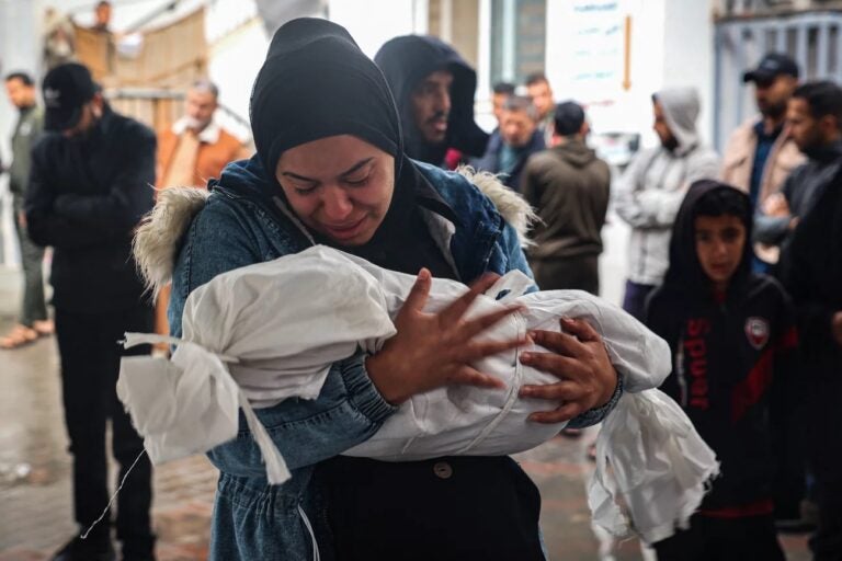 A woman mourns as she carries the shrouded body of a child killed following overnight Israeli strikes on Rafah in the southern Gaza Strip, on May 6. (AFP via Getty Images)